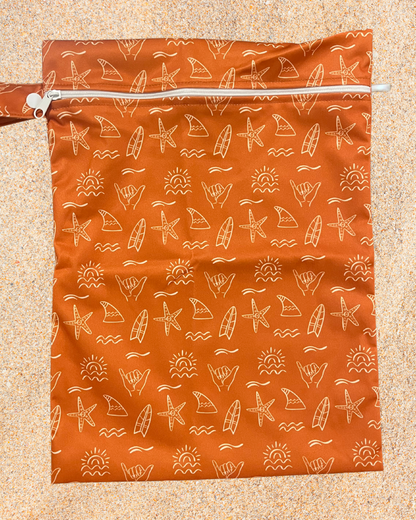 Orange zip wet bag with beach-themed pattern on a beige background