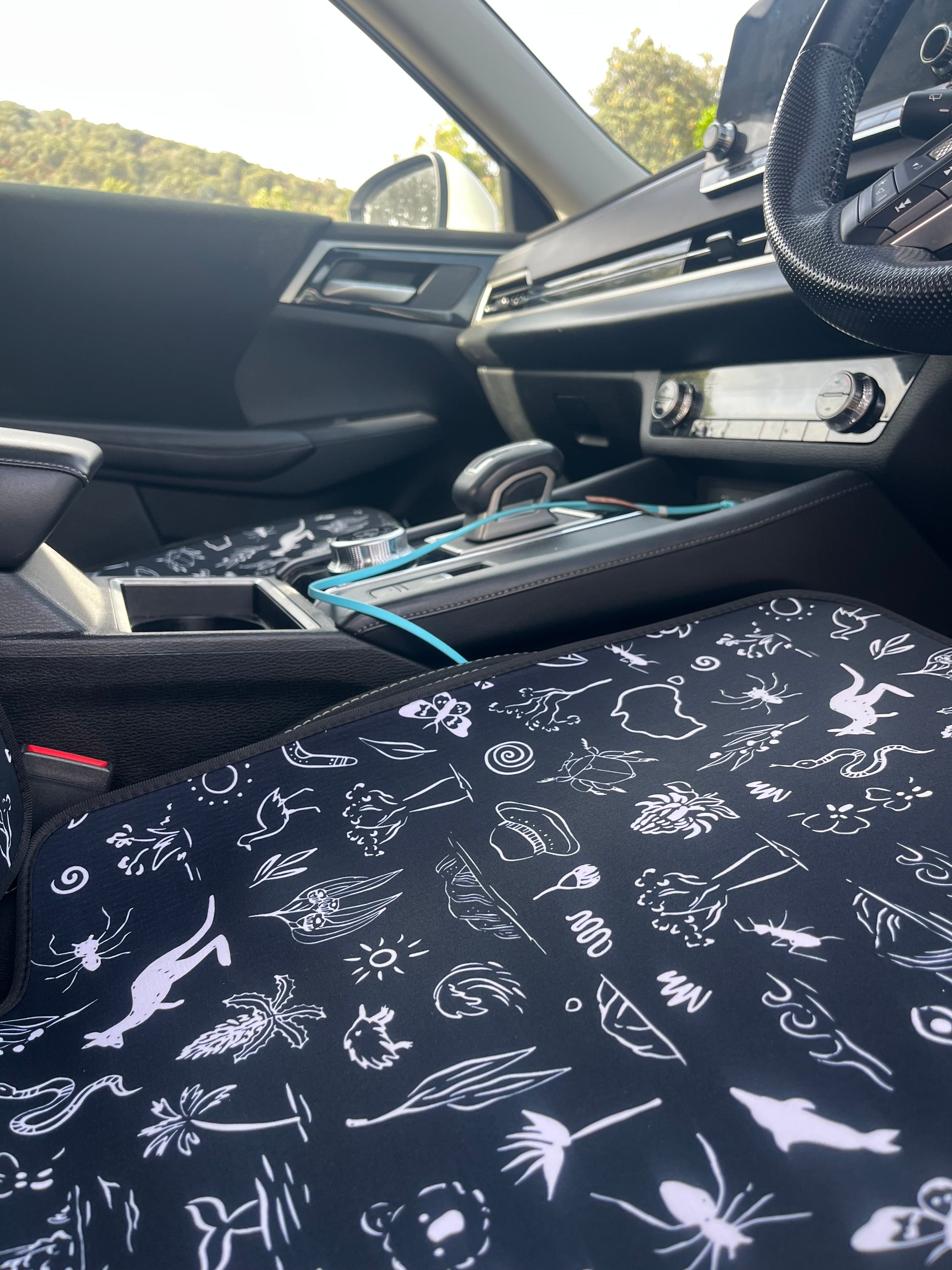 Car interior with a patterned seat cover featuring white illustrations on a dark background.