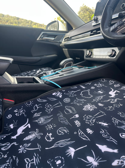 Car interior with a patterned seat cover featuring white illustrations on a dark background.