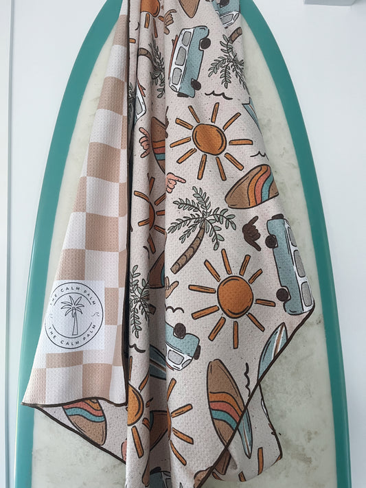 A beige seat towel with a beach-themed pattern, featuring illustrations of surfboards, suns, and beach chairs, displayed on a vehicle seat.