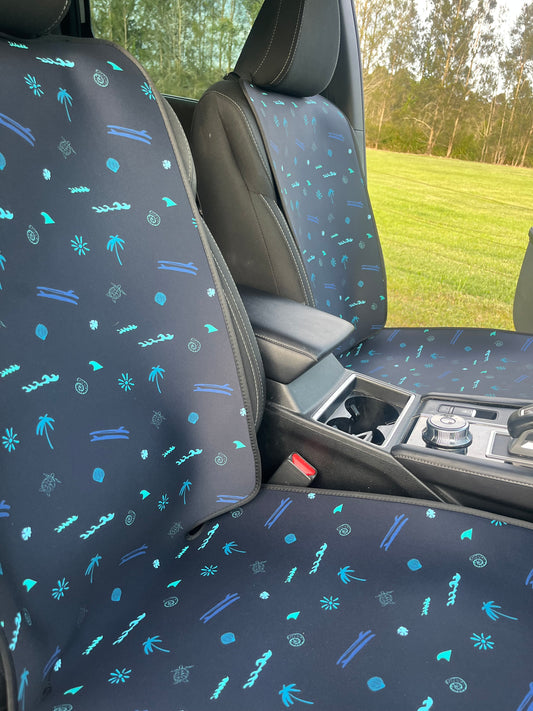 Car interior with patterned seat covers and a view of trees outside.