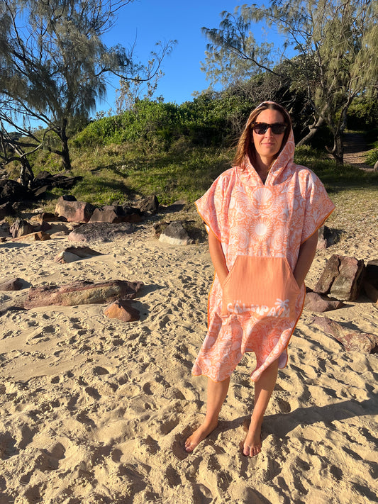 Person in an orange hooded towel standing on a rocky path with trees and blue sky in the background