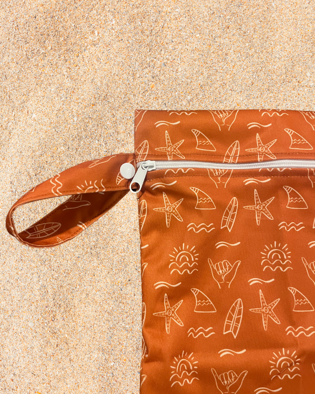 Orange wet bag pouch with white patterns on a sandy background