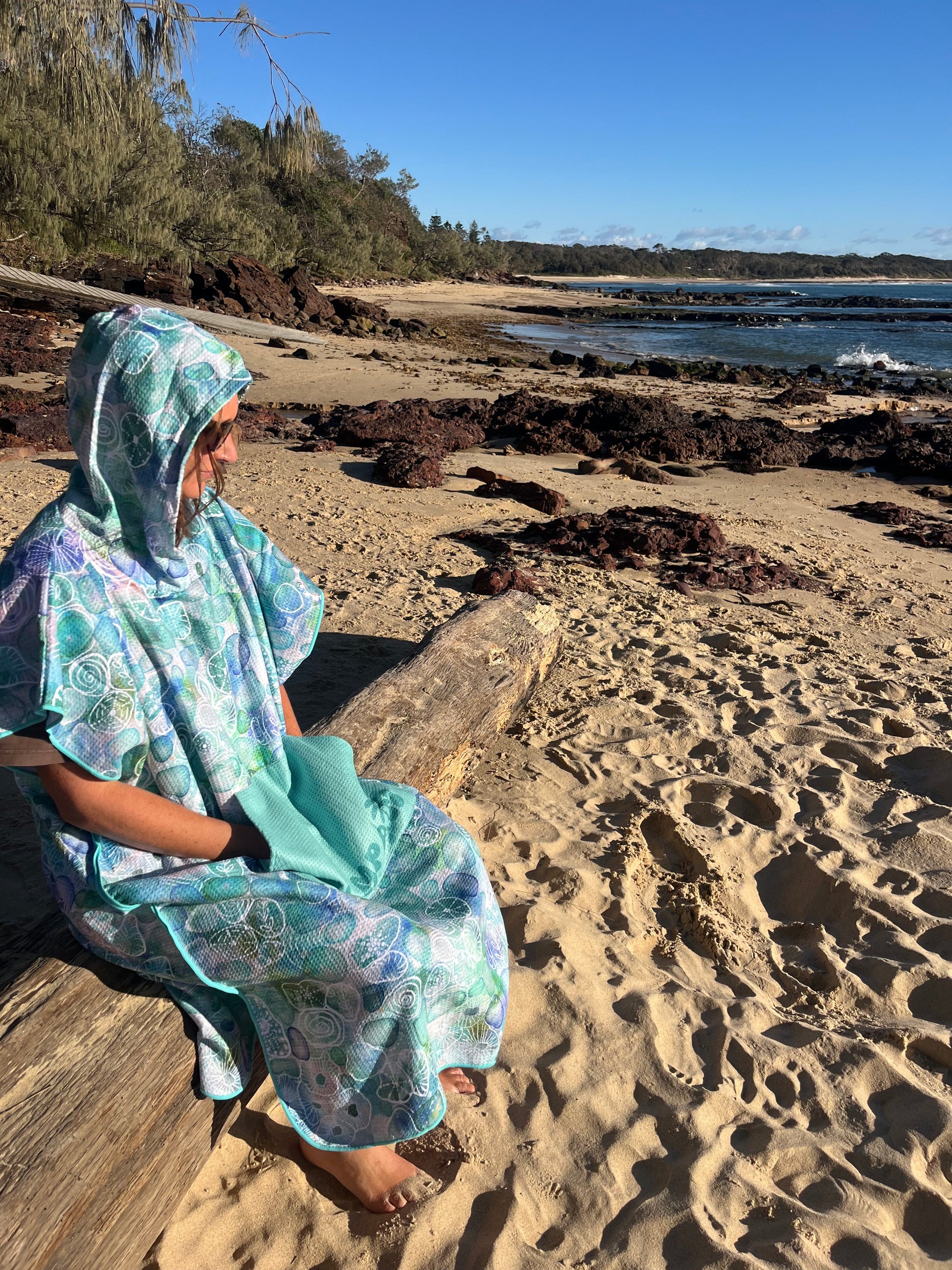 Person wrapped in a floral towel on a rocky beach