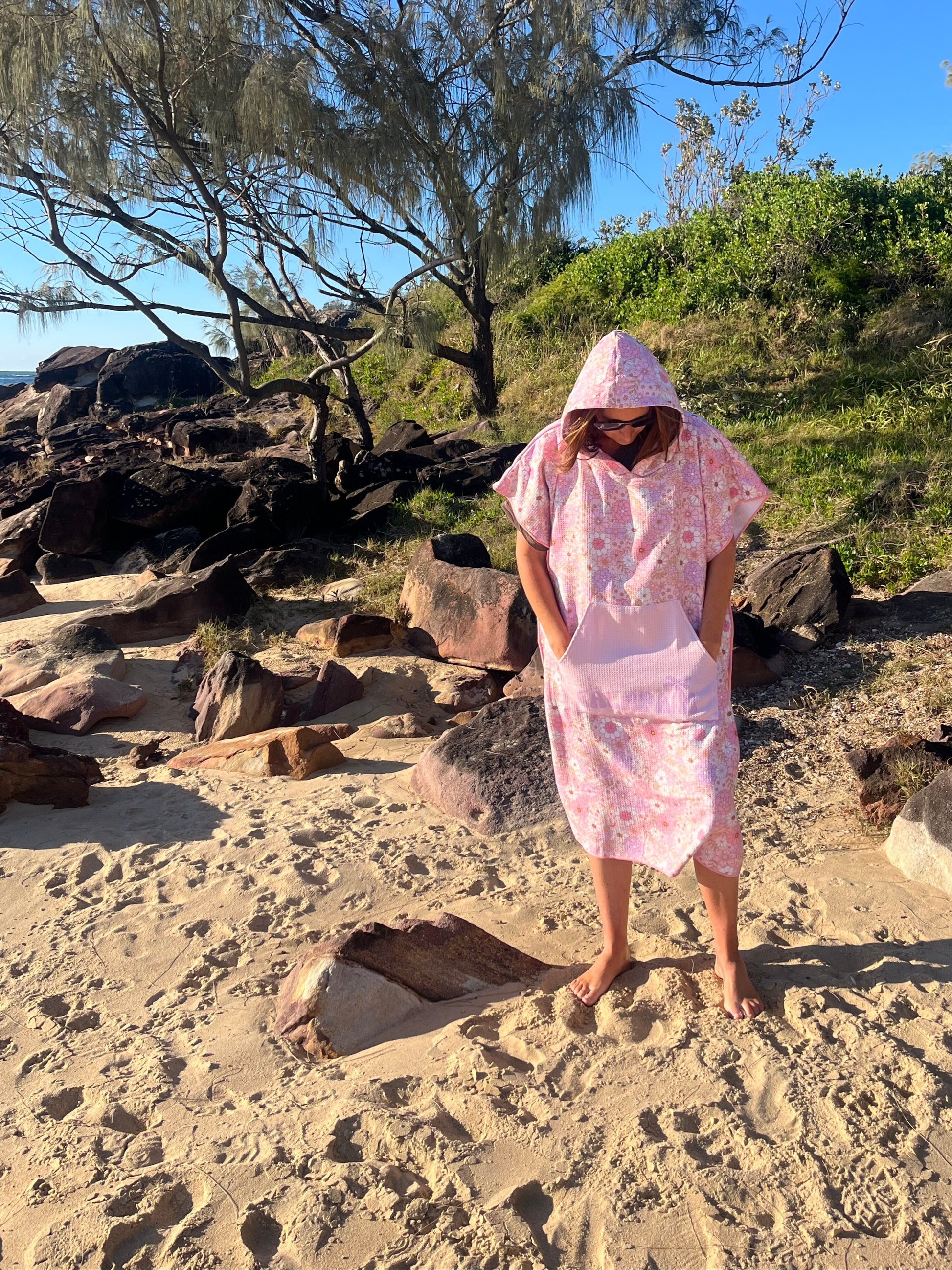 Person in a pink dress standing on a rocky beach with trees in the background