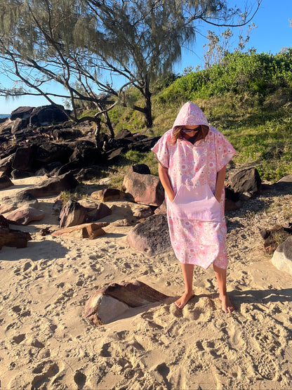 Person in a pink dress standing on a rocky beach with trees in the background