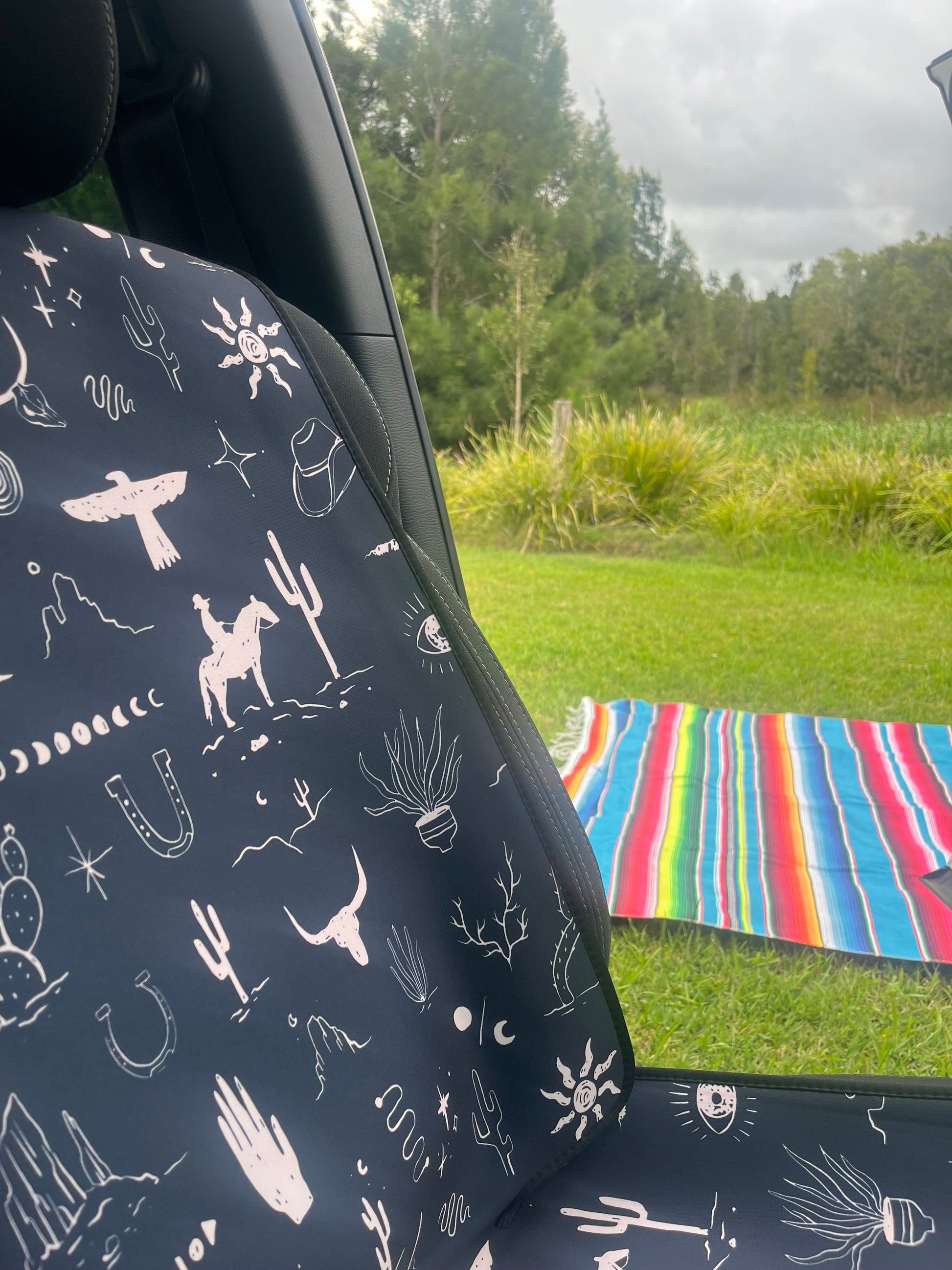 Set of black and white cowboy print Car Seat Cover shown on front car seats. Close up. Mexican rug in background of car