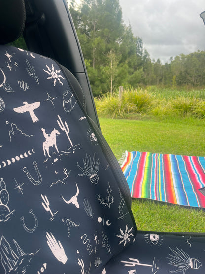 Set of black and white cowboy print Car Seat Cover shown on front car seats. Close up. Mexican rug in background of car